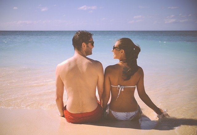 Žena a muž v plavkách sedia na pláži a majú nohy v mori.jpg